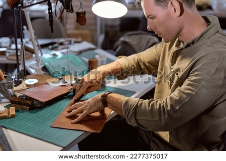 experienced leather worker concentrated on cutting material, close up side view shot.art of cutting leather, free time, spare time, hobby