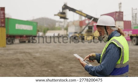 An experienced logistics foreman uses a tablet for supply chain management, coordinating cargo handling operations at a busy industrial shipping port.