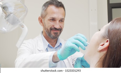 Experienced male dentist smiling while checking teeth of a patient. Handsome mature male dentist examining teeth of unrecognizable woman. Medical service concept