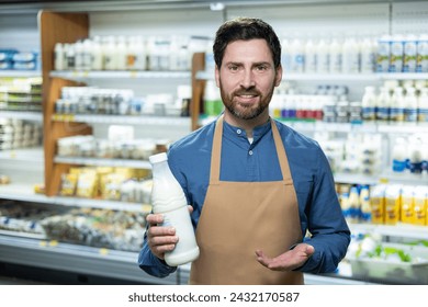 Experienced male employee in an apron stands in the supermarket's dairy section, suggesting a selection of milk and yogurts. The image captures the essence of daily grocery shopping and helpful - Powered by Shutterstock