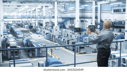 Experienced Male Engineer Standing on a Platform, Using Tablet Computer and Overlooking Production at a Modern Automated Electronics Manufacture with AI Support. Factory Executive at Work - Powered by Shutterstock