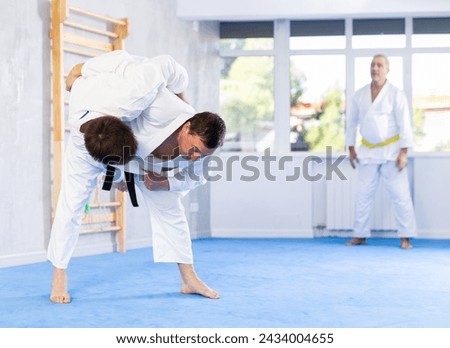 Experienced male karate instructor demonstrating attacking techniques in sparring with young martial arts fighter during training..