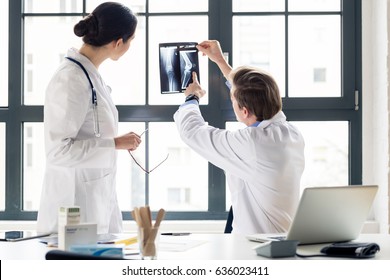 Experienced male orthopedist helping his female colleague with the interpretation of an X-ray of the knee of a patient in the office