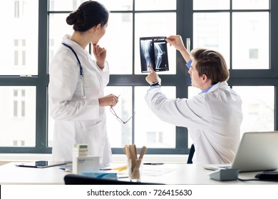 Experienced Male Orthopedist Helping His Female Colleague With The Interpretation Of An X-ray Of The Knee Of A Patient In The Office