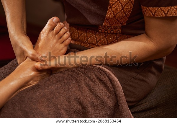 Experienced masseuse giving her client relaxing\
Thai foot massage