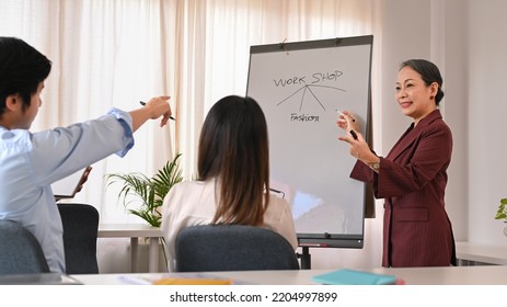 Experienced Mature Female Advisor Giving Presenting New Marketing Strategy To Young Employee In Creative Meeting