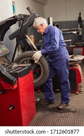 Experienced Mechanic In The Car Workshop With Tires During Repair Or Assembly