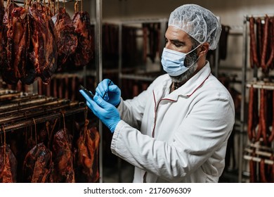 Experienced middle age man working in fresh meet processing plant. Industrial slaughterhouse worker job - dried meet quality check control. Food industry business concept. - Powered by Shutterstock