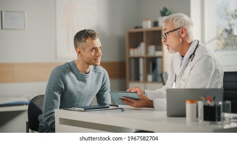 Experienced Middle Aged Family Doctor Showing Analysis Results on Tablet Computer to Male Patient During Consultation in a Health Clinic. Physician Sitting Behind a Desk in Hospital Office. - Shutterstock ID 1967582704