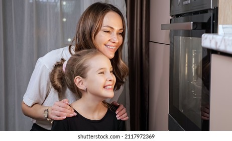 Experienced Mother Explains Teen Daughter In Black T-shirt Cooking Food Process In Stove Pointing To Glass Door In Home Kitchen Close View.