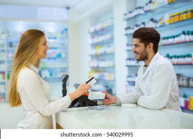 Experienced Pharmacist Counseling Female Customer In Modern Pharmacy, And Woman Pay With Credit Card