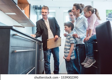 Experienced Salesman Showing Family The Features Of A New Kitchen