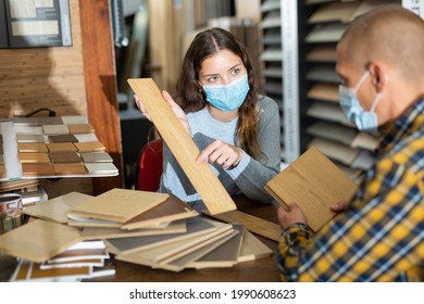 Experienced Salesperson In Protective Face Mask Working With Client Offering Laminate Flooring In Shop Of Building Materials