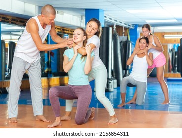 Experienced self-defense instructor teaching women to perform guillotine choke and to break free from choke hold during group training in gym