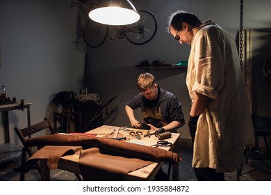 an experienced shoemaker and his assistant in their workshop make shoes from leather to order - Powered by Shutterstock