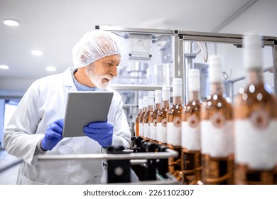 Experienced supervisor using digital tablet and controlling process of wine production in alcohol beverage bottling factory. - Powered by Shutterstock