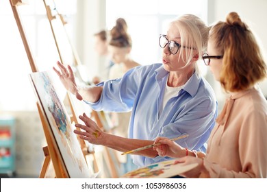 Experienced teacher consulting one of students about her painting during lesson in arts school - Powered by Shutterstock