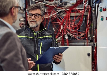 Experienced technician analyzing complex electrical wiring with clipboard in brightly lit workspace