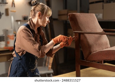 Experienced Woman Craftsperson Fixing Vintage Chair in Carpentry Workshop. Concept of repair and restoration old furniture. Side view - Powered by Shutterstock