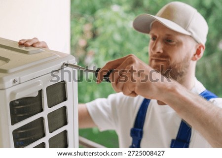 Experienced worker in blue overall using screwdriver, install ac. Worker maintenance and repair air conditioning unit outdoors, using tool, working outside the house