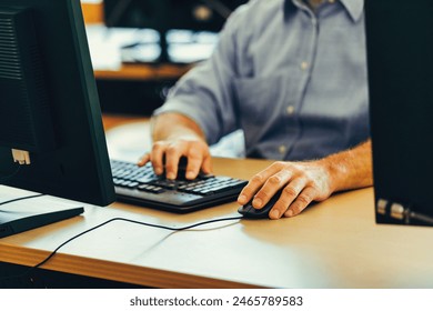 Experienced worker in a blue shirt focuses on a computer screen in an office, showing concentration and commitment to his tasks