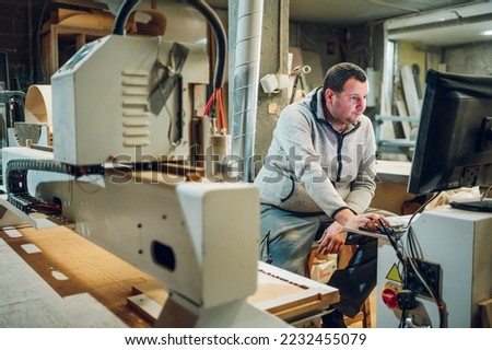 Experienced worker changing tool setup of CNC machine while working in a factory. Male machinery operator using industrial computer to work with and to program a CNC machine.