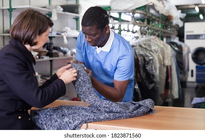 Experienced Worker Of Dry Cleaner Checking Clothes Of Female Customer On Reception..