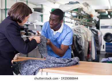 Experienced Worker Of Dry Cleaner Checking Clothes Of Female Customer On Reception..