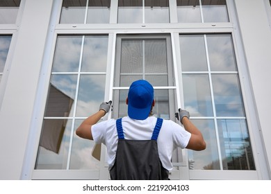 Experienced worker holds mosquito net in his hands, professionally installs it on window outside building. Professional installation of protective nets against insects on plastic windows of any size - Shutterstock ID 2219204103