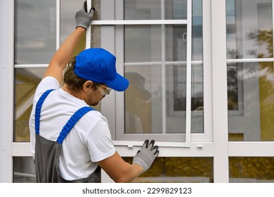 An experienced worker quickly and professionally puts a net on a plastic window in the summer. Wizard installs the mesh in the plastic fasteners on the white window