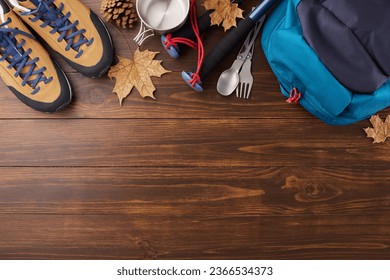 Experiencing the autumnal beauty on a hike. Top view shot of metal utensils, cozy footwear, hiking rucksack, trekking sticks, hat, cones, dry leaves on wooden background with ad zone - Shutterstock ID 2366534373