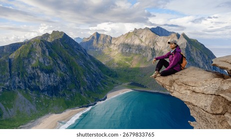 Experiencing natures majesty while sitting atop a rocky ledge, gazing at Kvalvika Beach and rugged mountains in Lofoten, Norway. The serene atmosphere and stunning landscape inspire adventure.