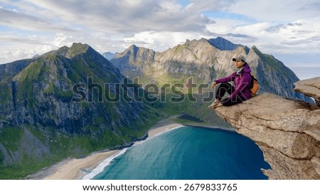 Experiencing natures majesty while sitting atop a rocky ledge, gazing at Kvalvika Beach and rugged mountains in Lofoten, Norway. The serene atmosphere and stunning landscape inspire adventure.