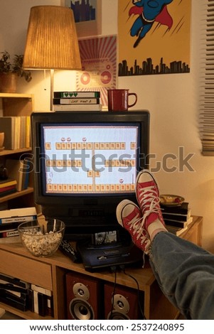 Experiencing nostalgia while playing game on retro television with feet propped up in casual red sneakers, surrounded by vintage decor and accessories