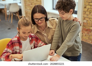 Experiment. Caring Young Female Teacher In Glasses Smiling While Helping Smart Kids To Learn Programming Using Laptop During STEM Class