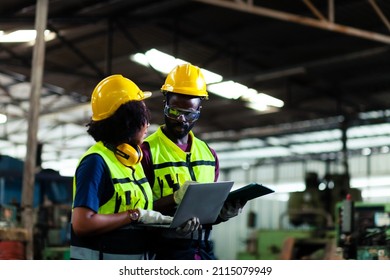 expert african engineer And an American woman walks in an industrial plant using a tablet to discuss the factory's black background mechanical work. - Powered by Shutterstock