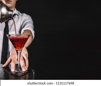 Expert barman making cocktail at nightclub.  Bartender preparing red cocktail at cocktail glass at the bar. Preparing of cosmopolitan cocktail. Red alcoholic drink in glasses on bar. 