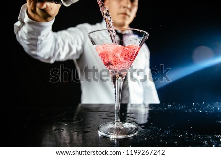 Expert barman making cocktail at nightclub. Bartender preparing martini at cocktail glass at the bar. Preparing of cosmopolitan cocktail. Pink alcoholic drink in glass on bar. 