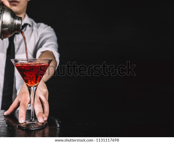 Expert\
barman making cocktail at nightclub.  Bartender preparing red\
cocktail at cocktail glass at the bar. Preparing of cosmopolitan\
cocktail. Red alcoholic drink in glasses on bar.\
