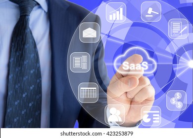 IT Expert In A Blue Suit Is Pressing A Glowing Cloud Symbol With SaaS, Software As A Service And Icons Of Services Around