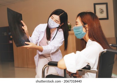 Expert Female Surgeon Shows A Physical X-ray To Explain To A Young Woman In A Wheelchair : Female Doctor And Patient Wearing Masks To Prevent The Spread Of Coronavirus In Hospital.