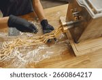 Expert hands skillfully roll out fresh pasta using a machine, emphasizing the beautiful artistry of home cooking