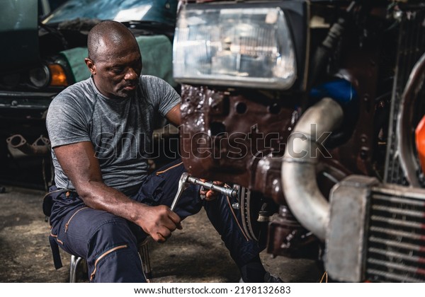 Expert male mechanic using a wrench\
to remove a steel wheel from car to repair in a\
garage.