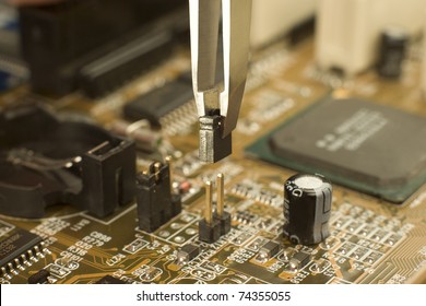 expert is putting electrical jumper on motherboard contacts with miniature forceps to lock electrical circuit