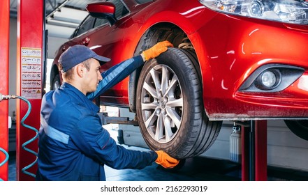 Expert specialist technician changes tires, tyres of lifted up car at auto service, wears uniform costume. - Shutterstock ID 2162293019