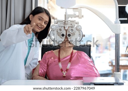 Expert is testing the vision test with diagnostic ophthalmology equipment, Indian or Nepali senior female customer looking through Optical Phoropter during eye exam