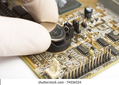 expert in white mitten on hand is putting round reflective battery with plus sign into computer motherboard