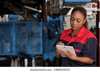 Expert young Black female automotive mechanic worker checks car's wheel brake disc and repairs inspect checklist by tablet at fix garage. Vehicle maintenance service works industry occupation jobs. - Powered by Shutterstock