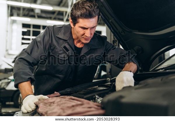 Expertise\
car mechanic in auto repair service. Car maintenance and auto\
service garage concept. Caucasian man working\

