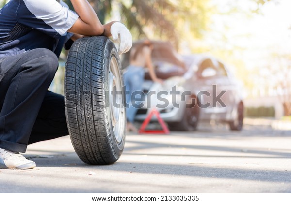 Expertise mechanic man in uniform holding a tire\
for help a woman for changing car wheel on the highway, car\
service, repair, maintenance\
concept.